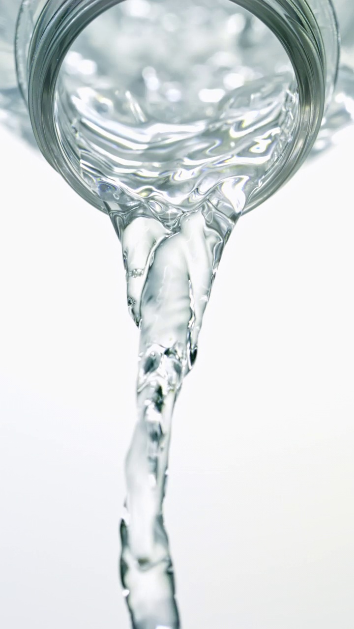 特写和超级慢镜头的瞬间，大量清澈的水从倾斜的透明水瓶喷口中流出，白色背景呈垂直形式视频素材