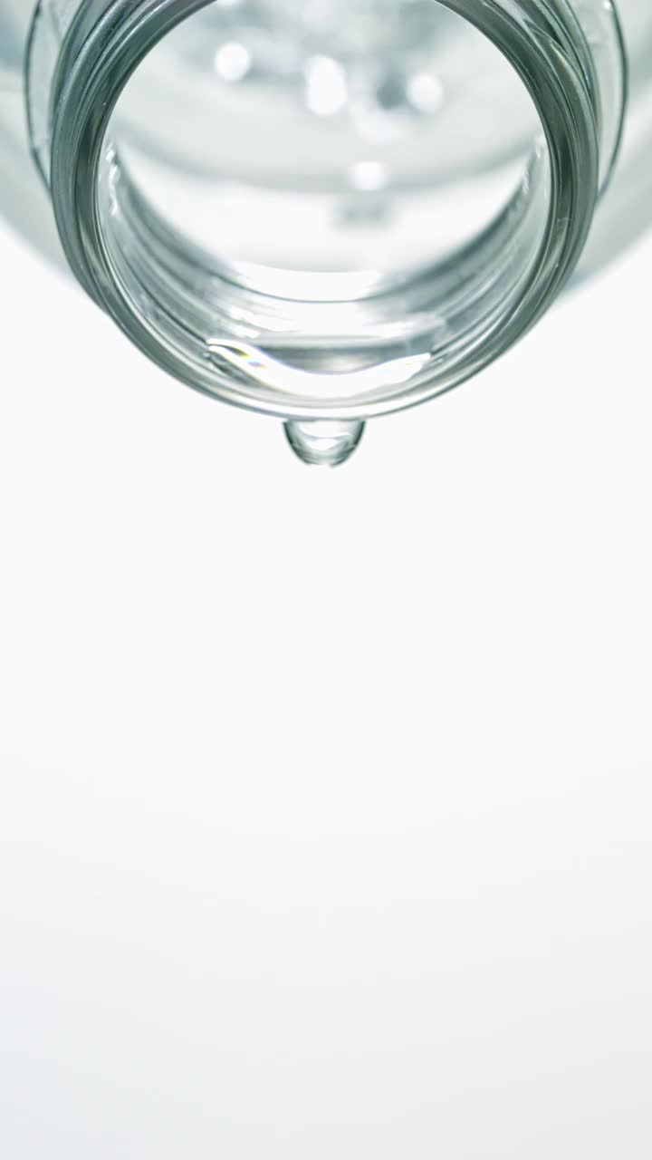 特写和超慢镜头的瞬间，大量晶莹剔透的水从倾斜的透明水瓶壶嘴中喷涌而出，在一个垂直的白色背景上视频素材