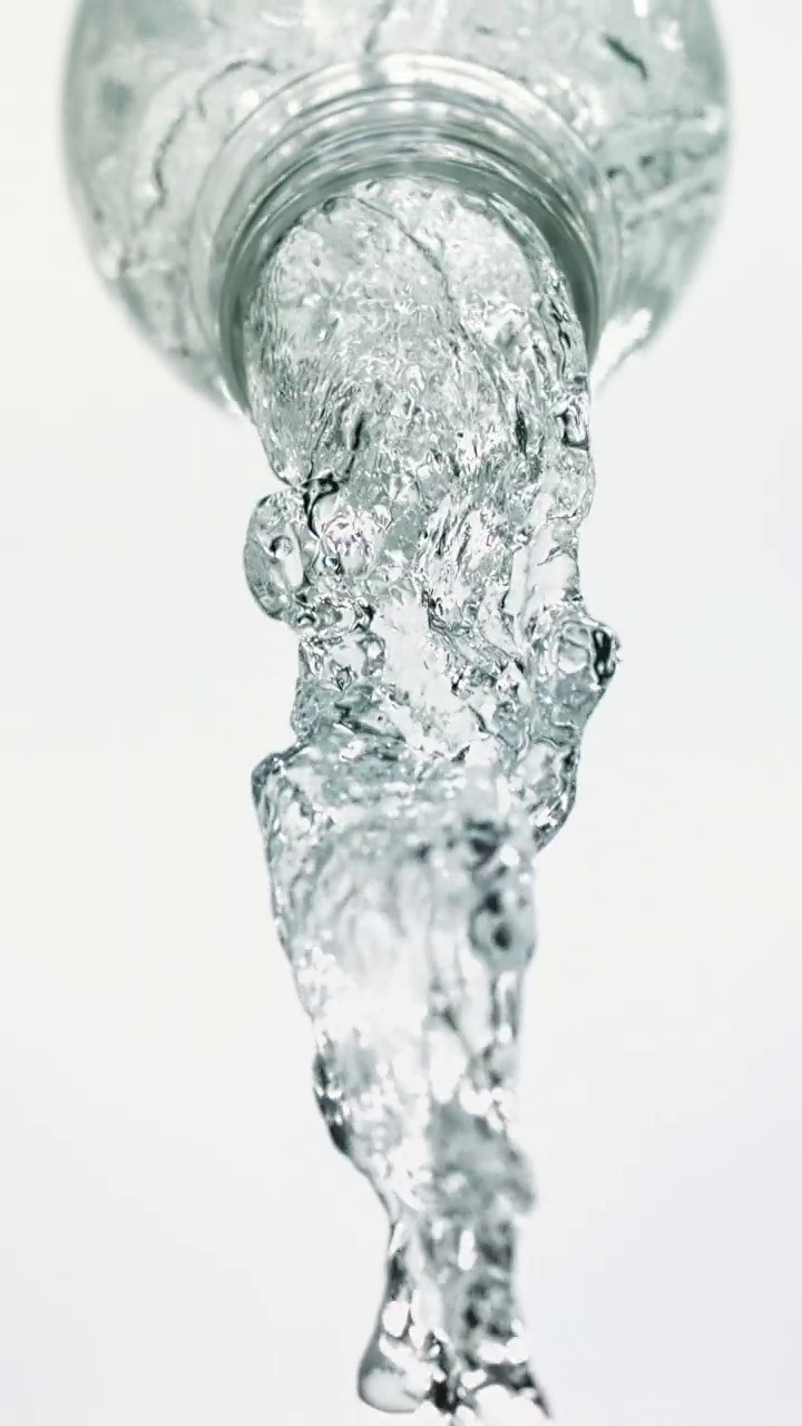 特写和超慢镜头的瞬间，清澈的水溅出来，大量的水从倾斜的透明水瓶喷口流出，白色背景呈垂直状视频素材