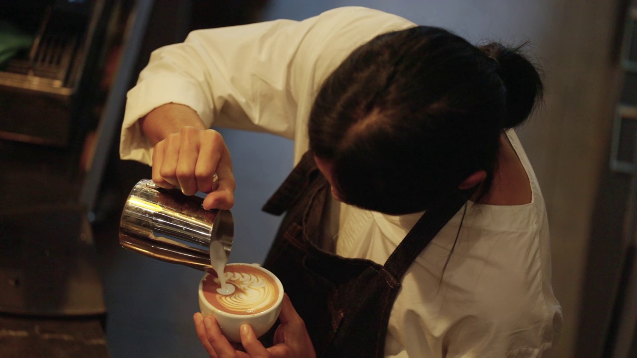 4K亚洲男子咖啡师倒泡沫牛奶在浓咖啡咖啡咖啡拿铁咖啡杯。视频下载