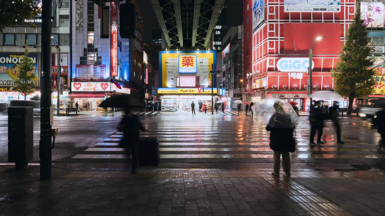 时间流逝的雨夜，日本东京秋叶原电力城，人们打着伞走十字路，汽车交通运输。、游戏、娱乐区。亚洲旅游，或亚洲旅游视频下载