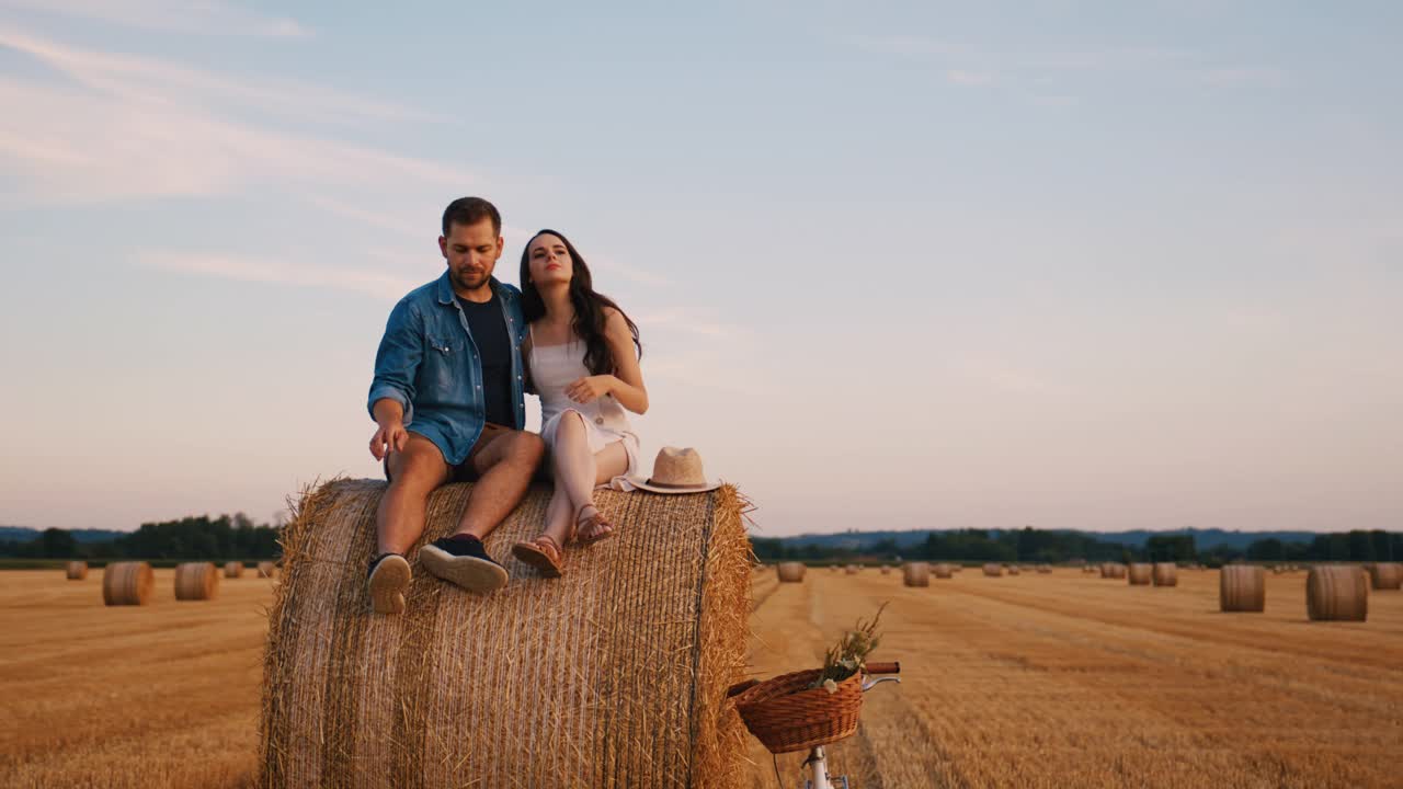 手持慢动作镜头，中年夫妇坐在田间的干草堆上拥抱，享受日落视频素材