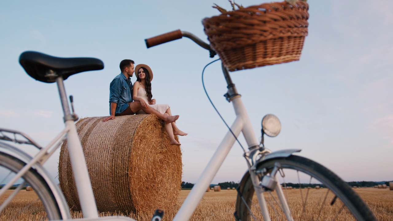 手持慢动作镜头，中年夫妇坐在干草堆上，前景是自行车，享受日落视频素材