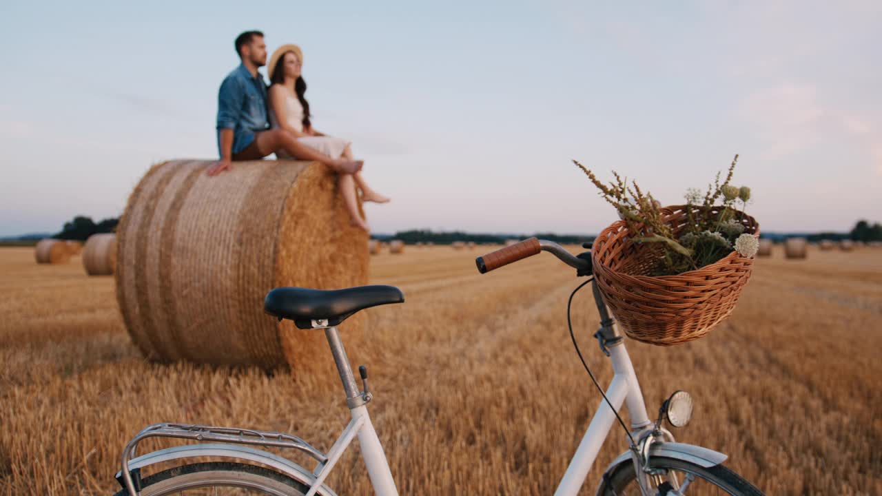 手持慢动作镜头，中年夫妇坐在干草堆上，前景是自行车，享受日落视频素材
