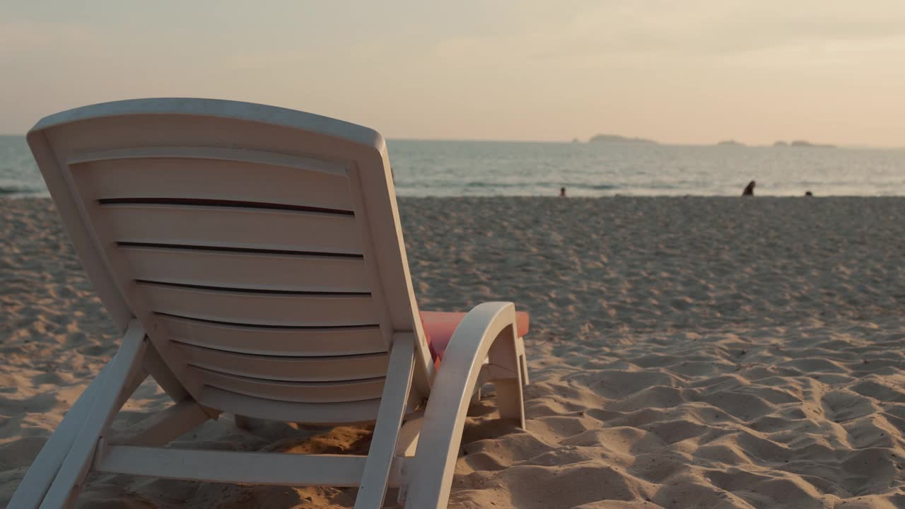 在夏季美丽的日落天空、海洋和地平线下，沙滩上的沙滩椅的慢镜头4K显示了在热带岛屿放松的惊人假期的概念。视频下载