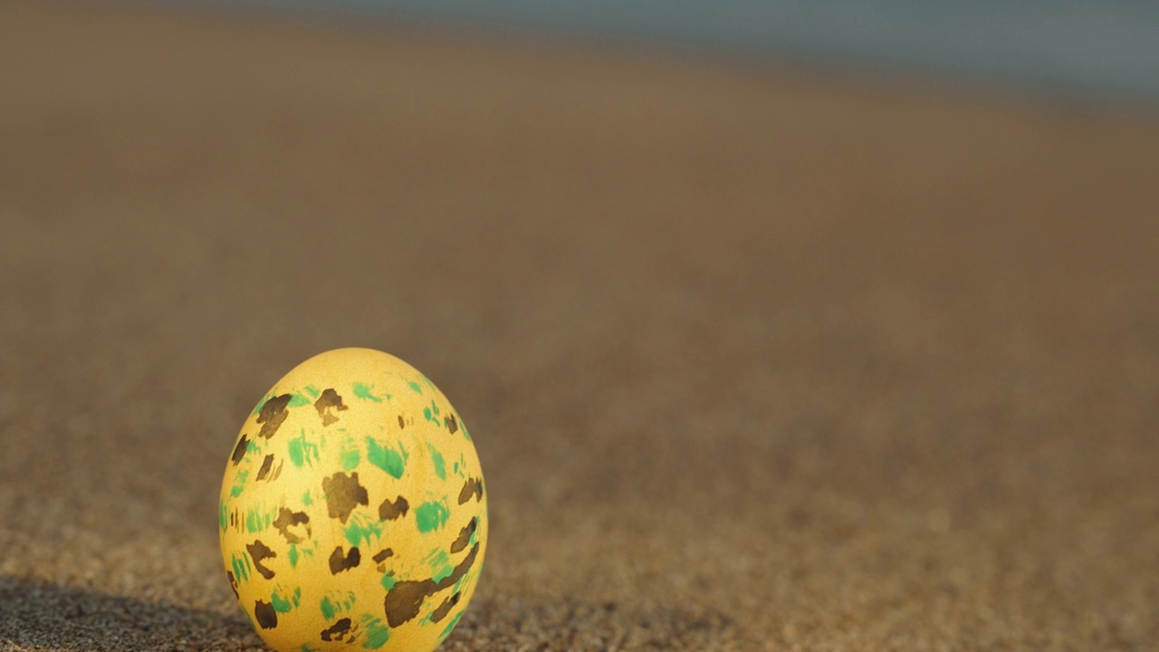 沙滩上黄色装饰的复活节彩蛋，特写。焦点转移到海浪上视频下载