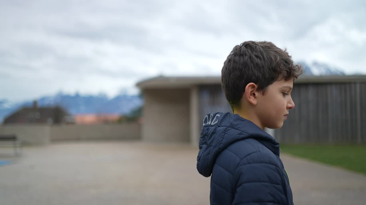 一个沉思的小男孩站在外面思考。穿着冬装的孩子站在城市公园沉思。严肃的表情视频素材