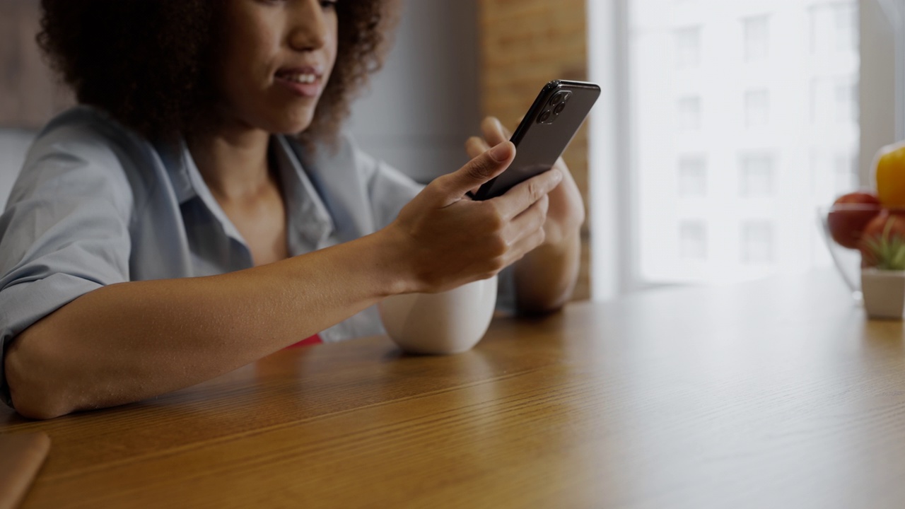 一个非裔美国妇女用智能手机在早上喝咖啡的特写镜头视频素材