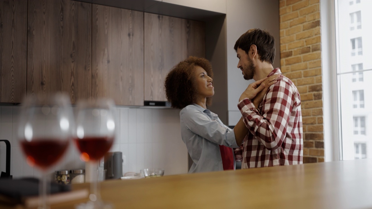 年轻女子和她的男朋友在家里跳舞，桌上放着酒杯，浪漫视频素材