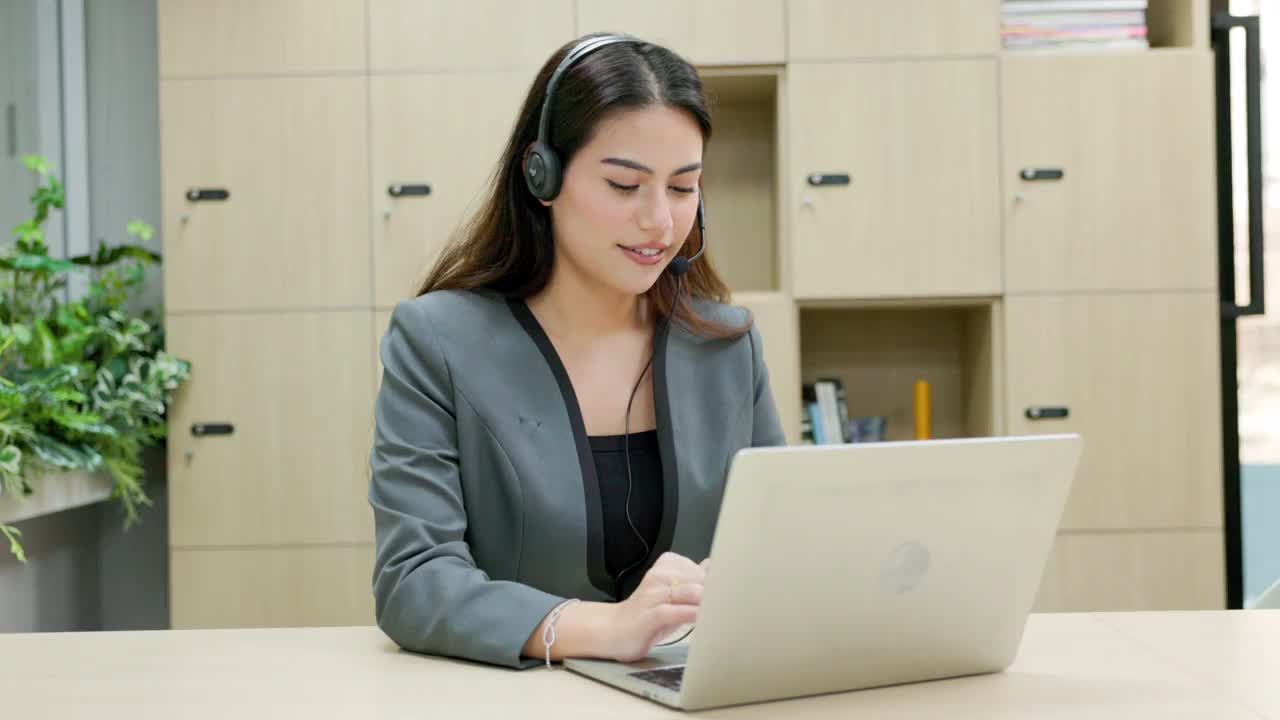 年轻的女商人戴着耳机和使用电脑。客户服务代表和呼叫中心在家工作的概念:广角和手持拍摄视频下载