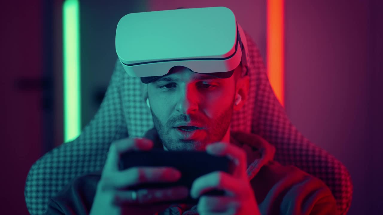 快乐的家伙男人玩家穿着竞争玩视频游戏在线与智能手机彩色霓虹灯在客厅在晚上现代的房子。电竞在线直播游戏，居家隔离活动。视频下载