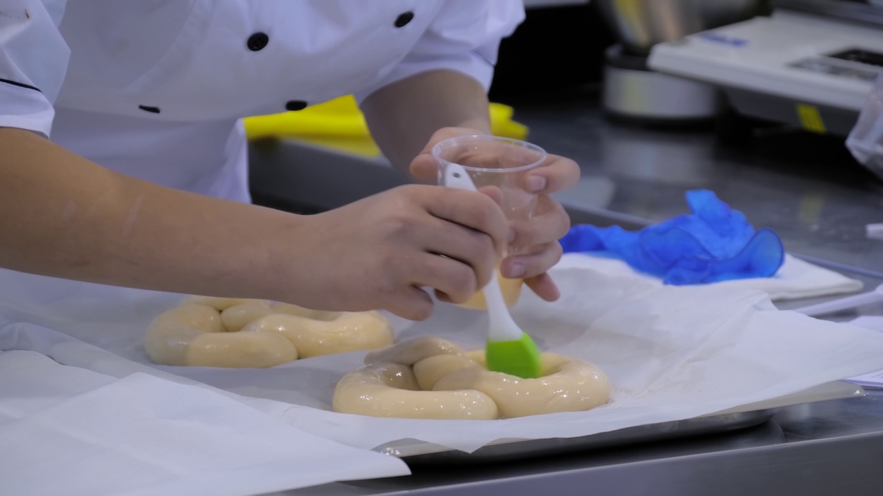面包师用手将液体鸡蛋涂在新鲜的面团上做辫子面包-特写视频下载