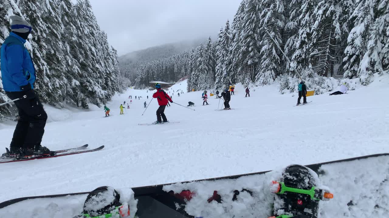 第一人称视角:业余滑雪者和滑雪板运动员在滑雪场的滑雪坡上滑下来，很多滑雪者在冬天在山上滑雪视频素材