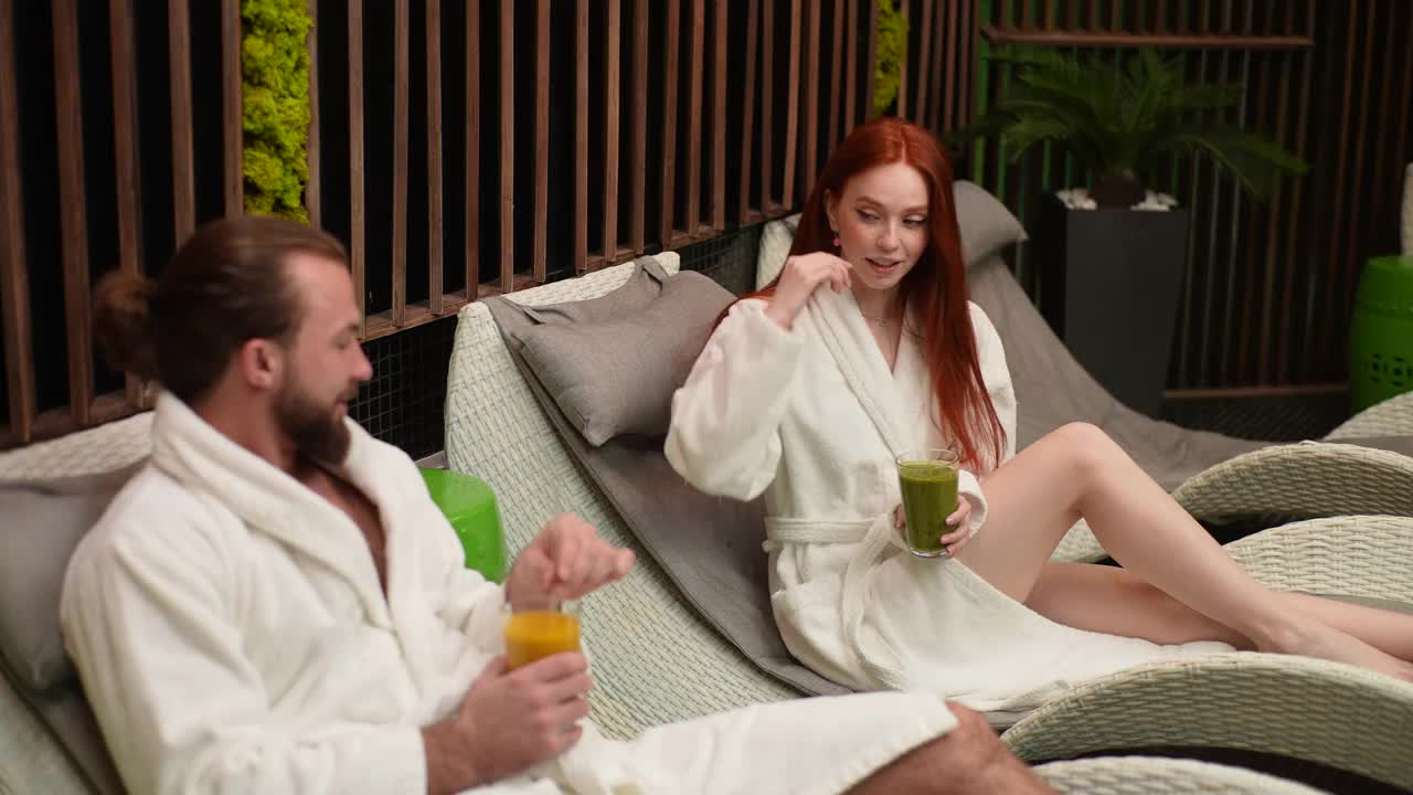 年轻的白人夫妇在温泉治疗后在游泳池的躺椅上调情的中景镜头。视频下载