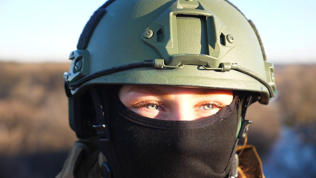 近距离看日落的年轻女军人的蓝眼睛。乌克兰女士兵头戴头盔，头戴巴拉克拉瓦帽。入侵乌克兰领土。欧洲战争结束视频下载