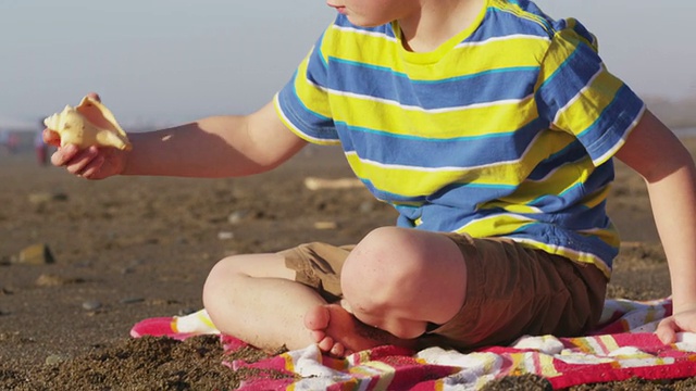海滩上的男孩捡起贝壳听着视频素材