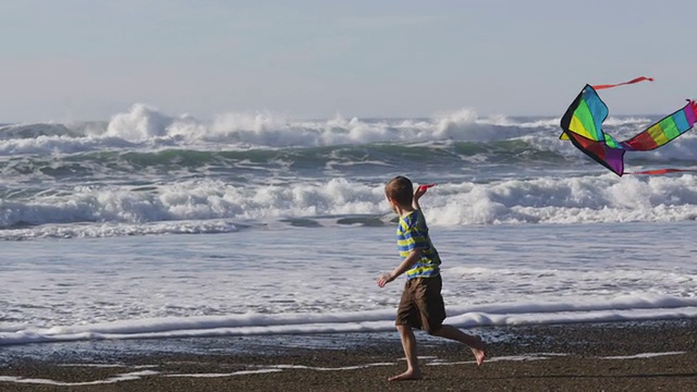 小男孩拿着风筝在海滩上奔跑，慢镜头视频素材