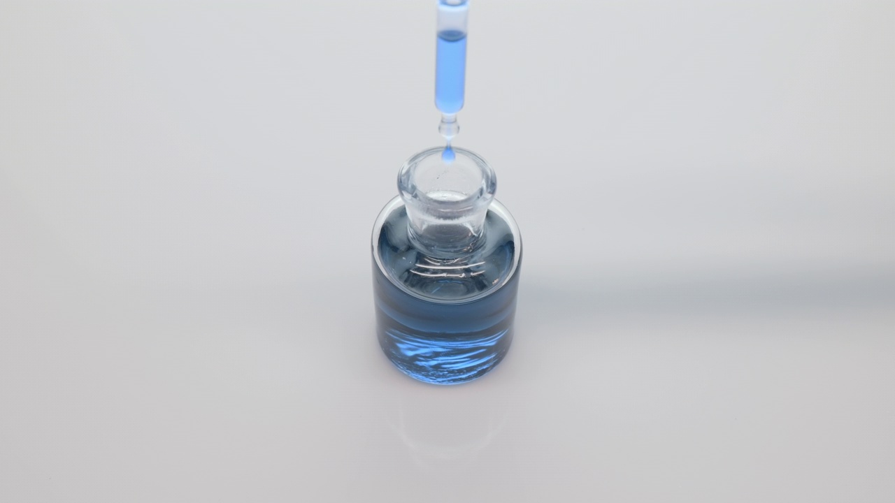实验室滴管将蓝色丁香花油滴入灰色背景的瓶子中视频下载
