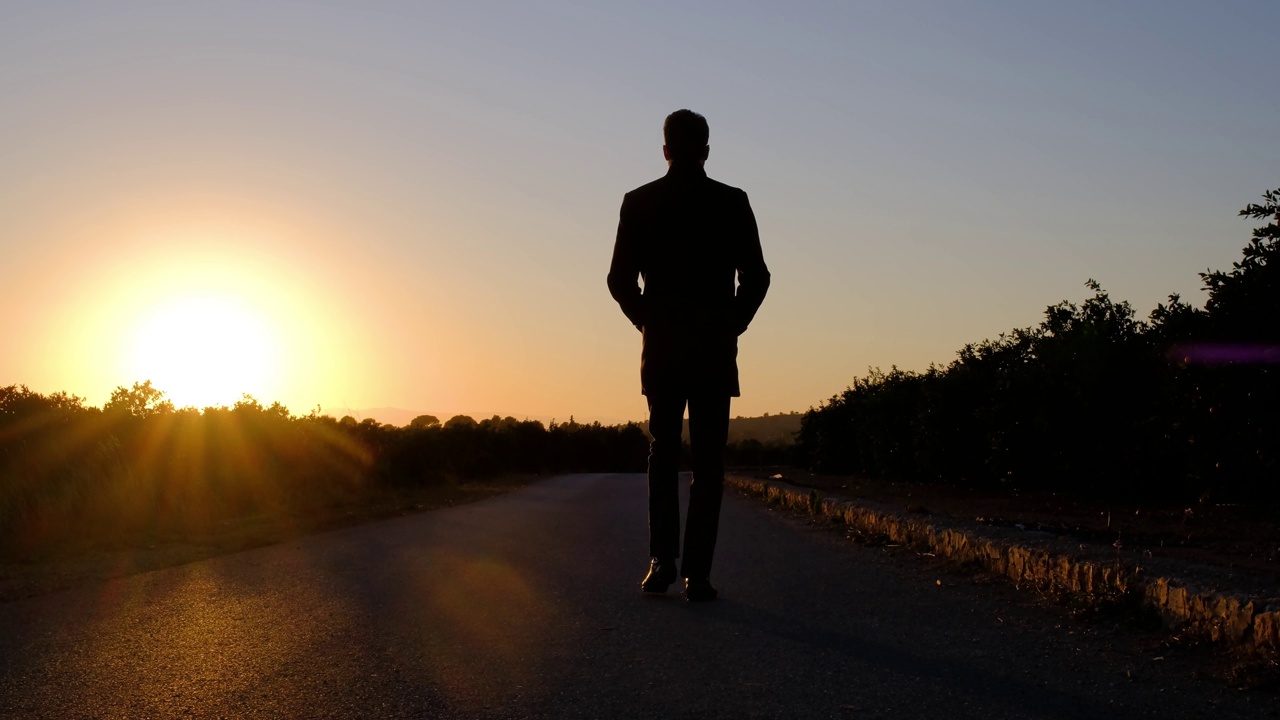 在金色的夕阳下，一个男人的剪影走在路上。视频下载