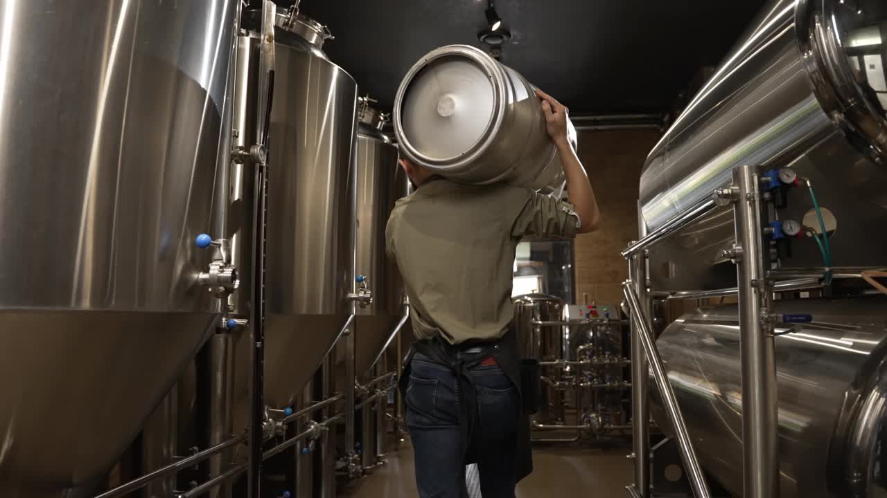 一名男性酿酒工人提着装满啤酒的酒桶经过啤酒罐视频下载