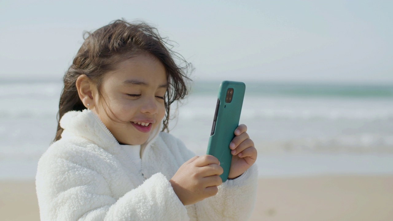可爱的亚洲女孩拿着智能手机在她的小手视频下载