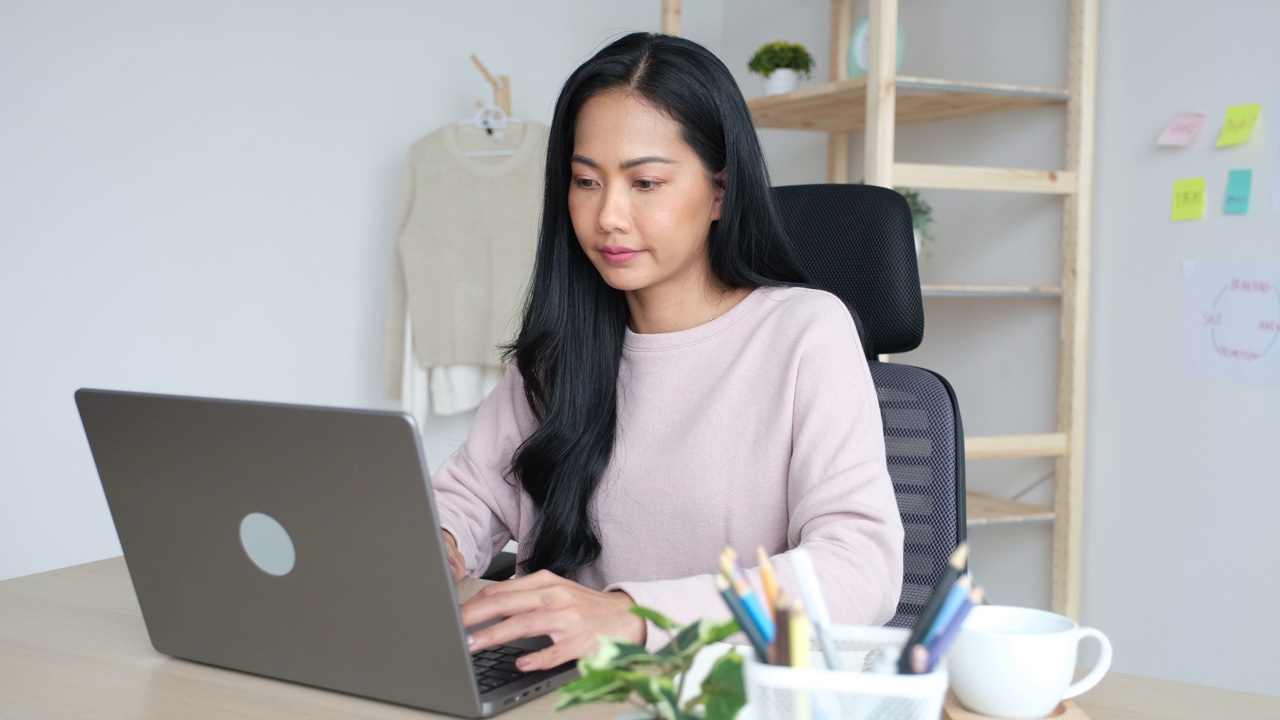 年轻的亚洲妇女使用笔记本电脑，而坐在家里的办公室视频素材