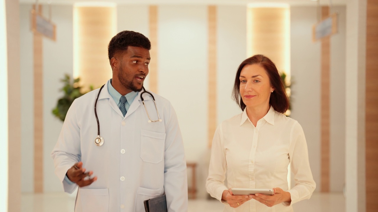 一名年轻的非洲医生在医院走廊里和一名白人女医生一起给病人看病。视频素材