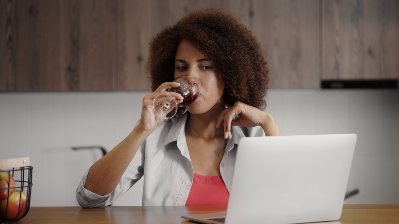 微笑的女人享受葡萄酒和独处的时间，在笔记本电脑上看电视节目视频素材