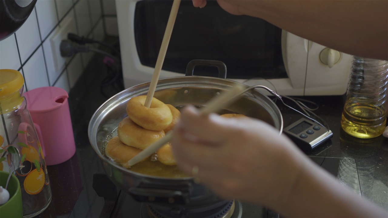 一个女人的手用筷子在油炸甜甜圈后舀起。视频素材