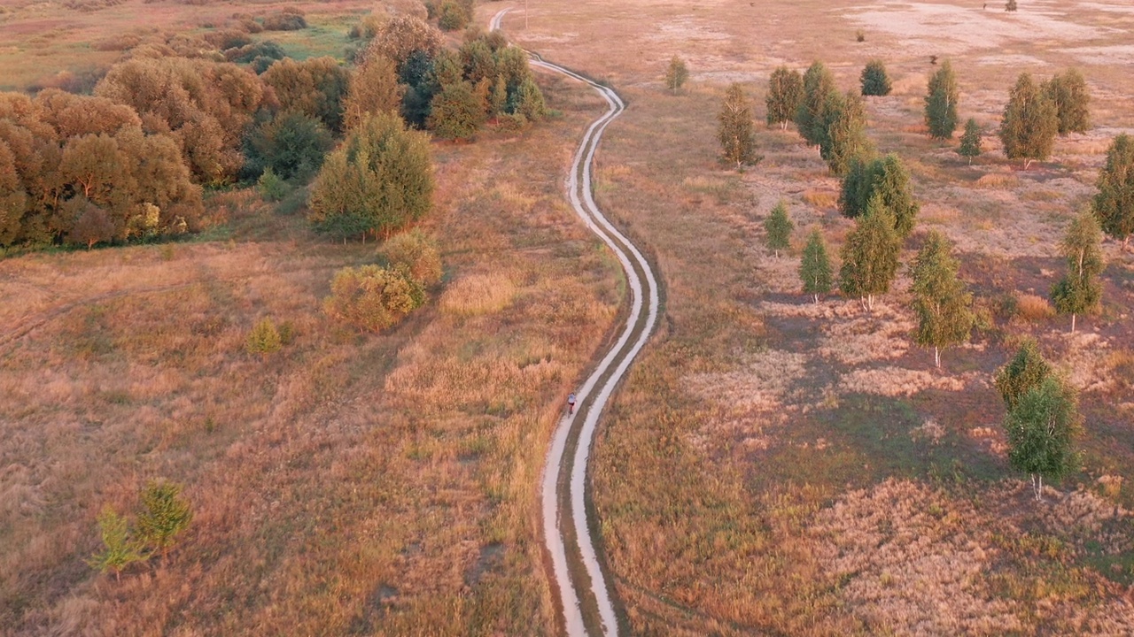 空中俯视图的自行车骑在乡间与弯曲的道路在田野。视频下载