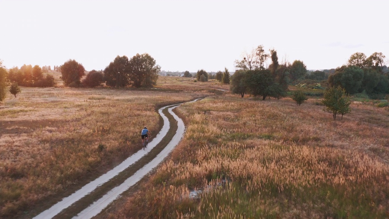 日落时分，骑自行车的人沿着田野里的越野公路骑自行车。视频下载