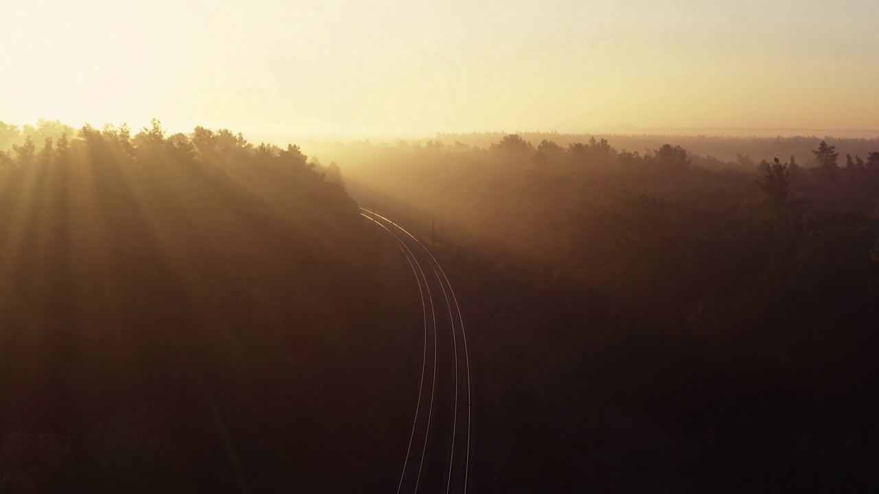 铁路轨道在雾蒙蒙的秋天森林与明亮的阳光。鸟瞰图。视频下载