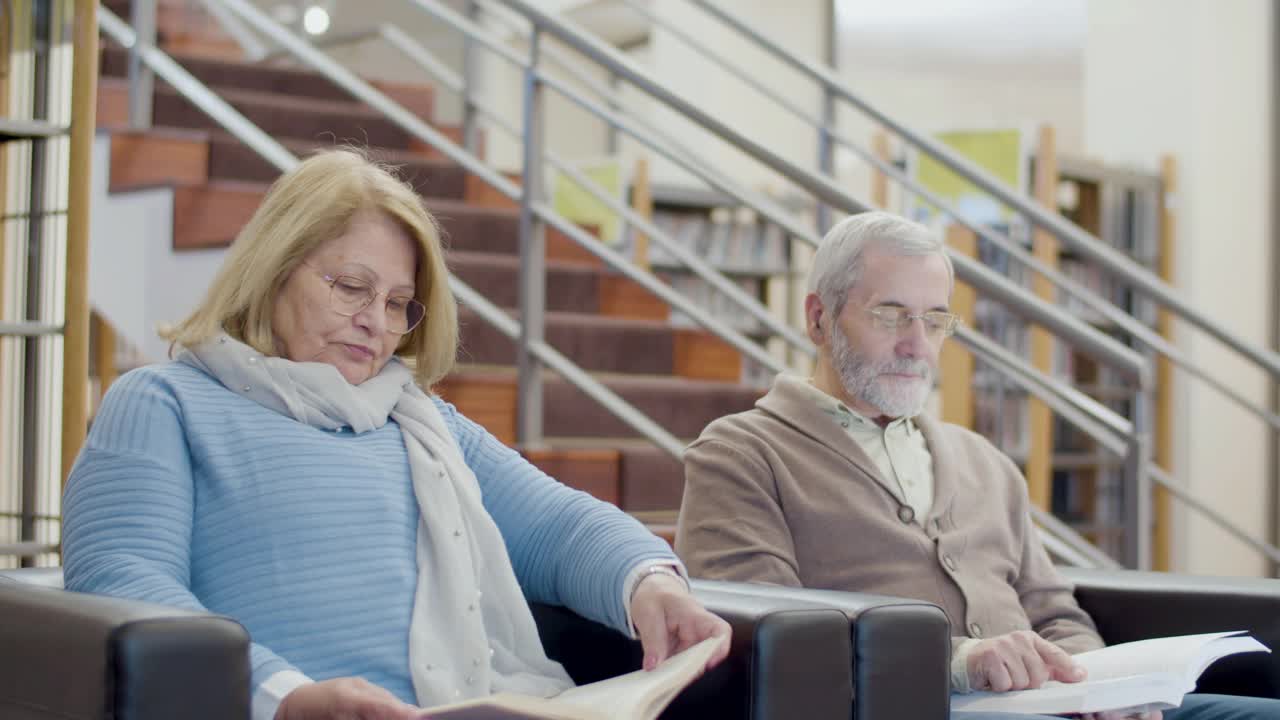 专注的高级男性和女性坐在图书馆的扶手椅上视频下载