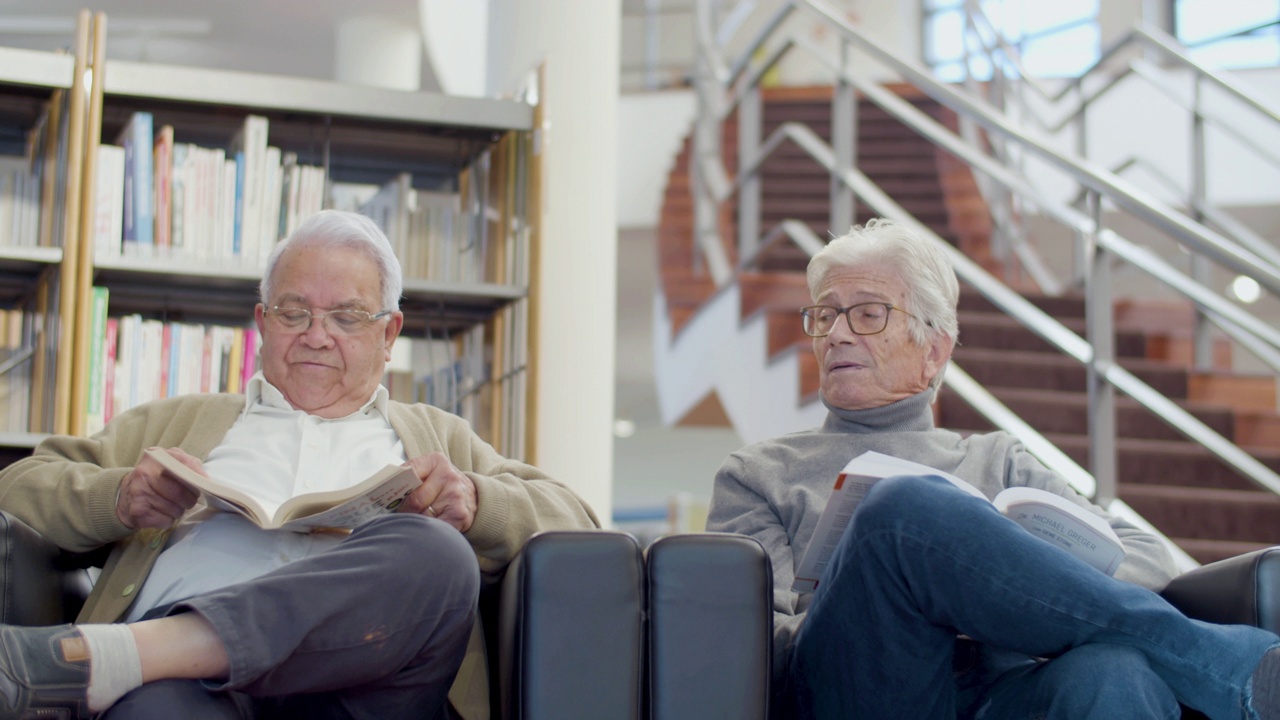 愉快的前辈朋友坐在图书馆的扶手椅上视频素材