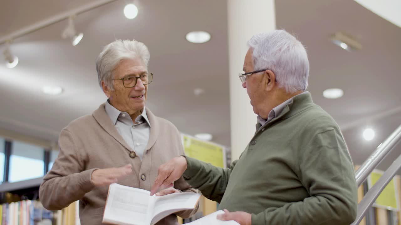 白发苍苍的老朋友在公共图书馆讨论书籍视频下载