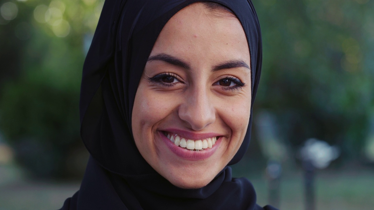 美丽的年轻阿拉伯妇女微笑的肖像与绿色的背景。快乐的穆斯林女运动员与希贾布在公园享受新鲜空气在她的清晨锻炼视频下载