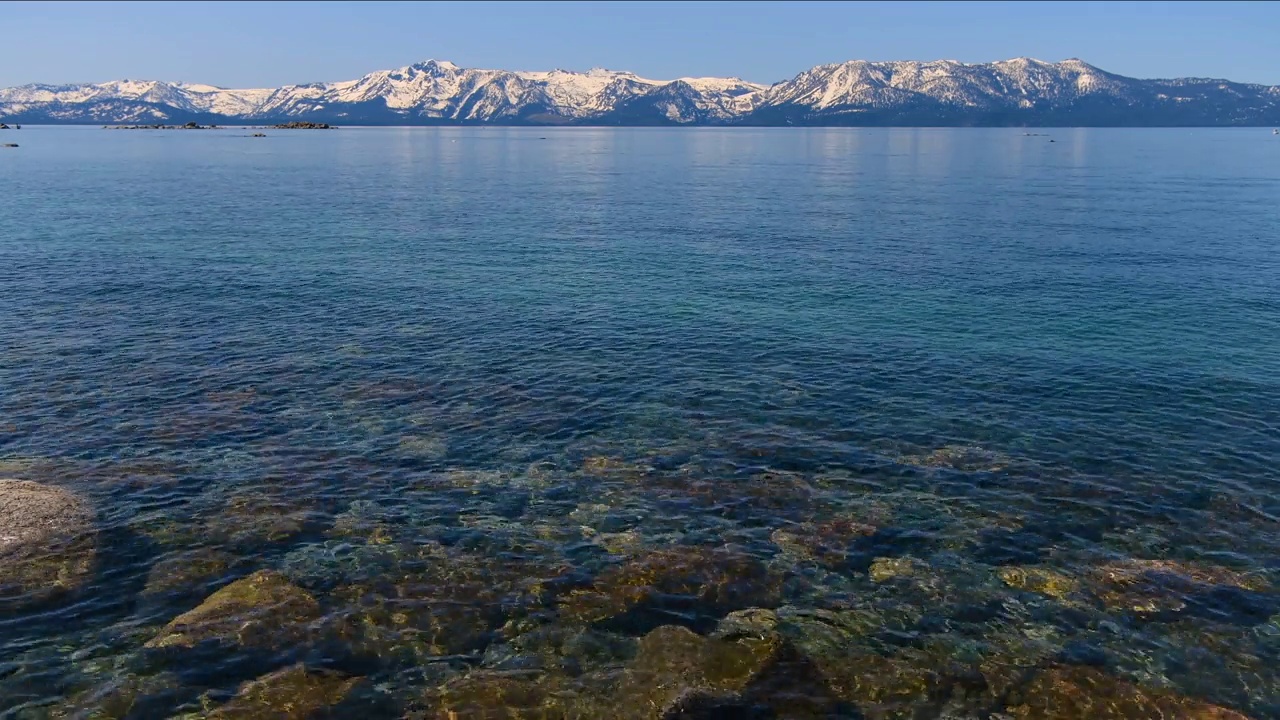 太浩湖——太浩湖清澈湛蓝的湖水特写，地平线上高耸的内华达山脉积雪覆盖的山峰。太浩湖，加利福尼亚州，美国。视频下载