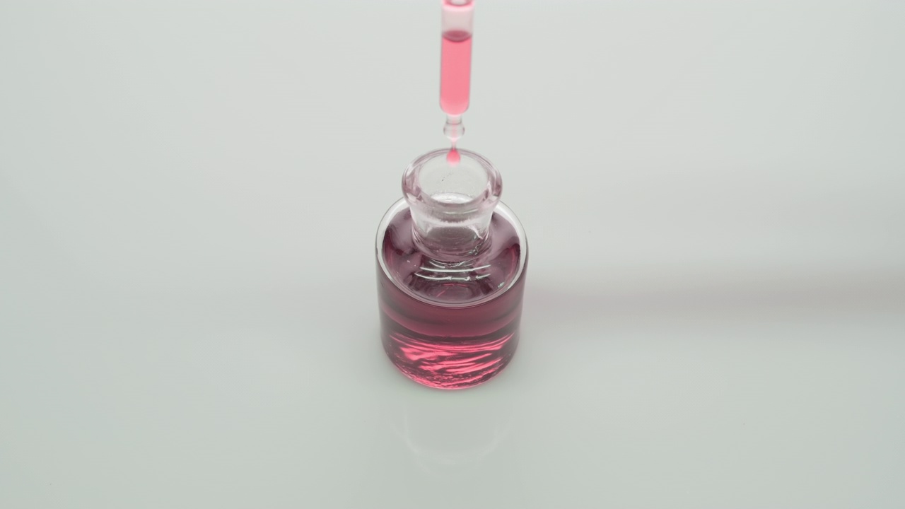 实验室滴管将玫瑰水滴入灰色背景的瓶子中视频下载