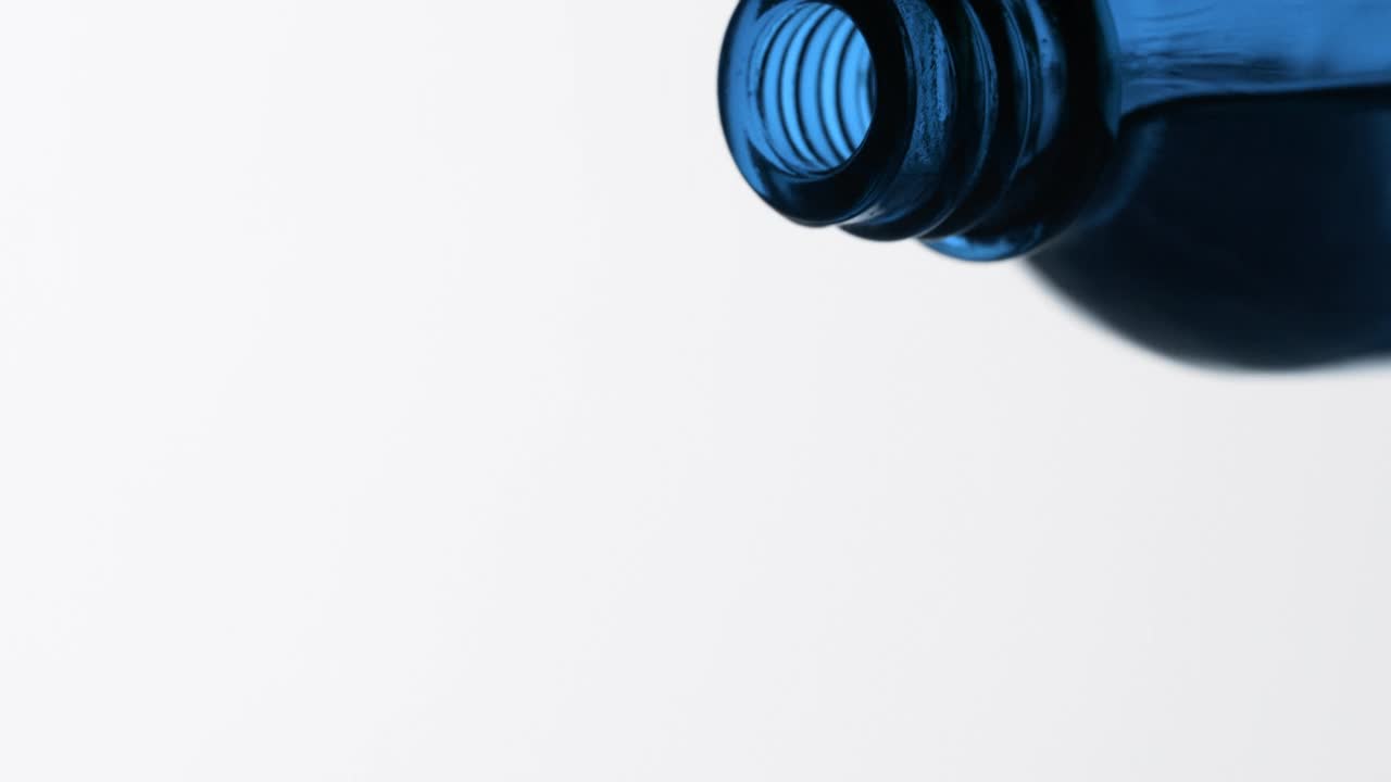 蓝色的唐茜油从蓝色的瓶子倒在灰色的背景视频素材