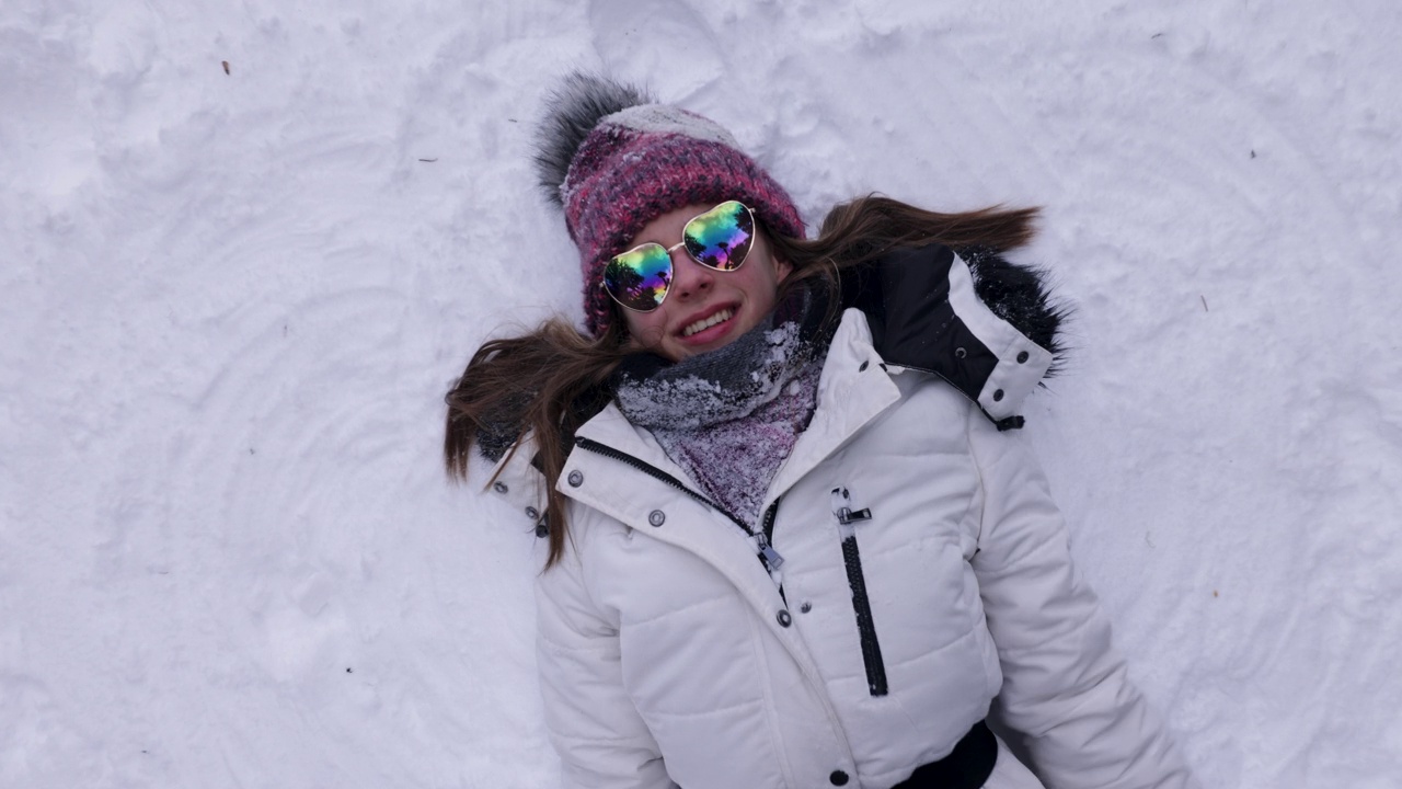 十几岁的女孩戴着心形太阳镜，享受在雪地里做雪天使视频下载