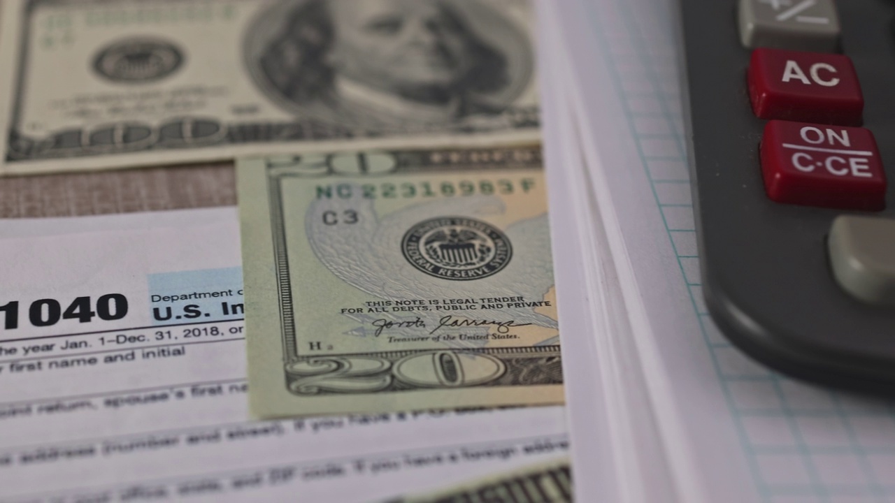 美国公民的桌上放着一张美元钞票、一个笔式计算器和一张美国1040个人税单。视频素材