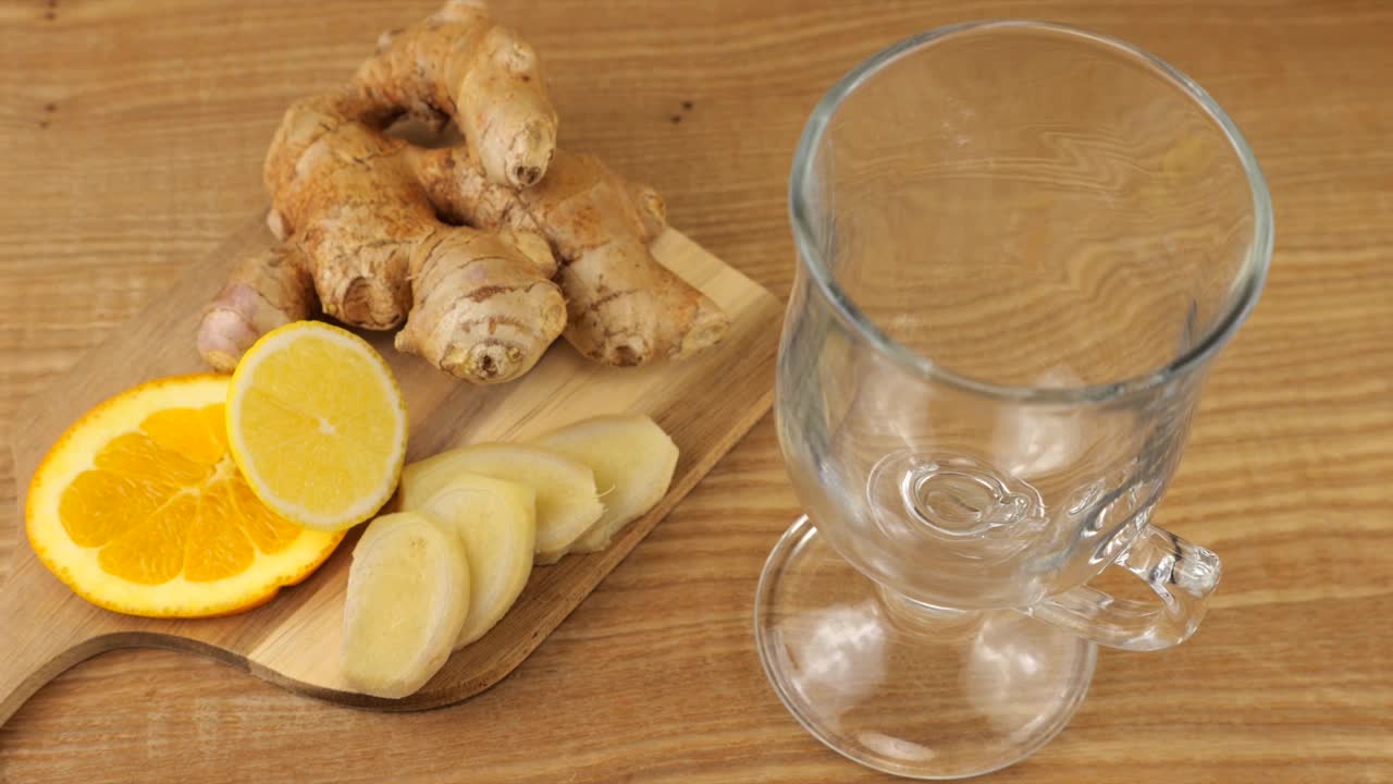 煮柑橘和生姜饮料来增强免疫力。柠檬水被倒入玻璃杯中，背景是橘子片、柠檬片和姜片。缓慢的运动。视频下载