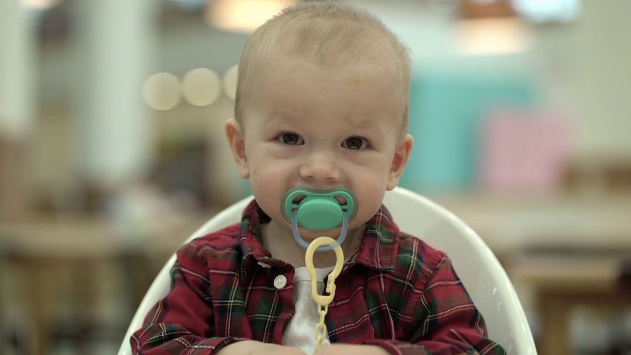 一个小孩坐在婴儿椅上，吮吸着奶嘴。视频下载