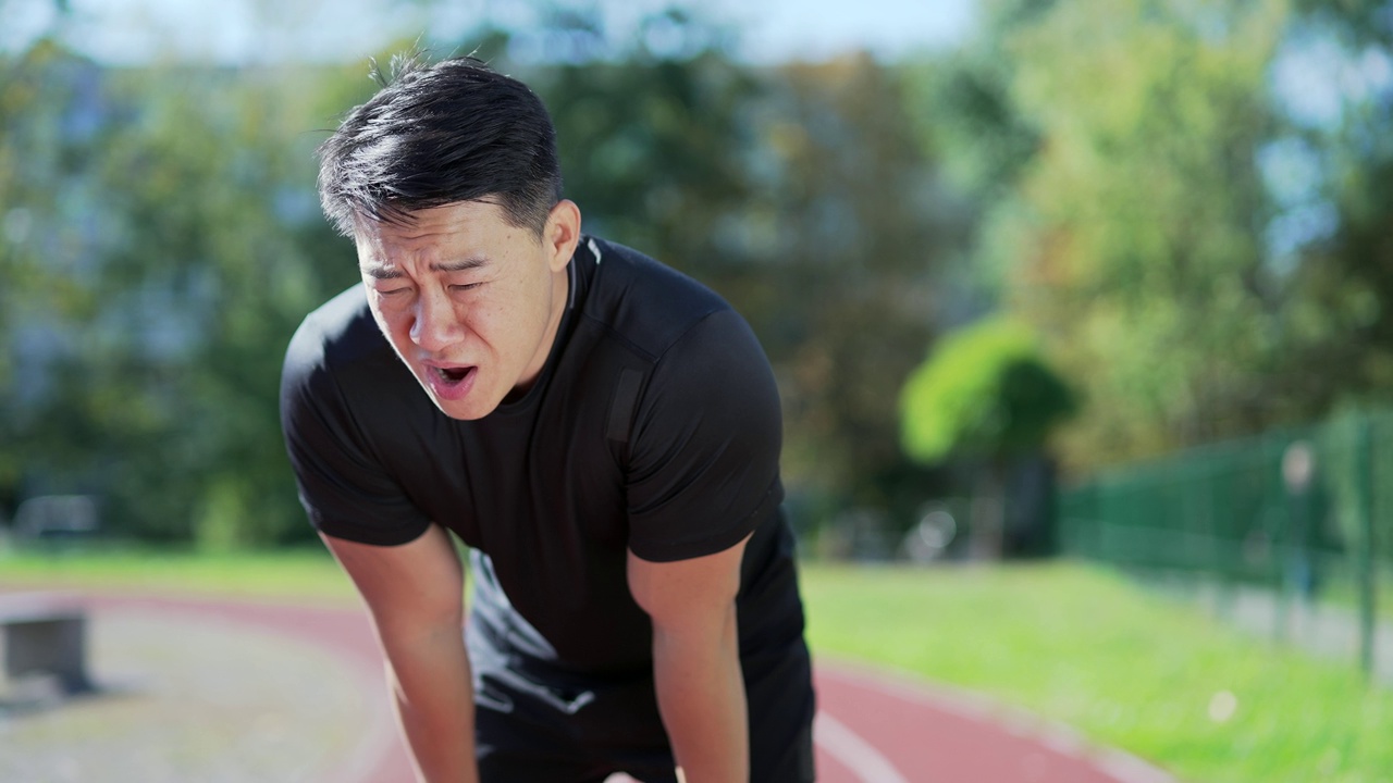 一名成年亚洲运动员在城市体育场的跑步机上快速冲刺后呼吸急促。一个穿着运动服的运动员斜着身子视频下载