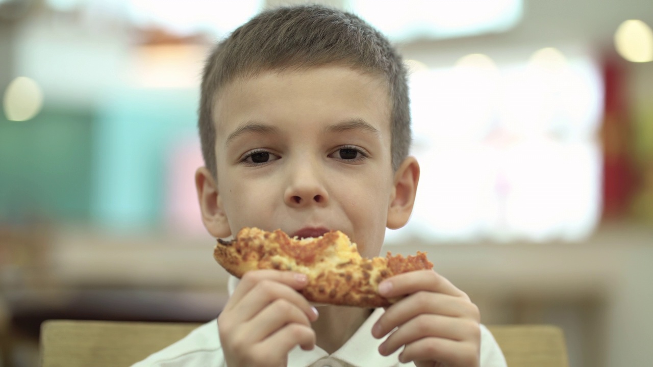 图为一个男生坐在美食广场的桌子旁吃着一片披萨视频下载