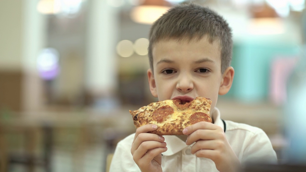 孩子吃不健康的食物。男孩在快餐店吃饭。吃披萨的快乐男生。视频下载
