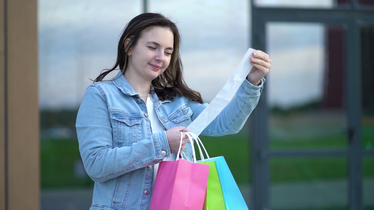 在购物中心购物后，年轻女子看着现金收据上商品的价格视频下载