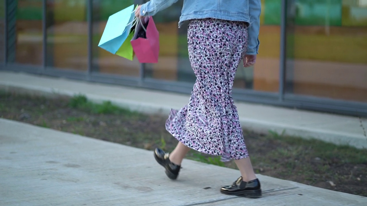 一个穿长裙的女人手里拿着纸袋走在人行道上视频下载