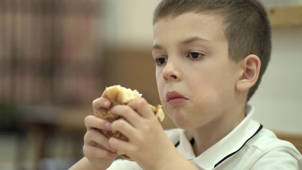 男孩喜欢在快餐店吃东西，手里拿着汉堡，开心地咬着它视频下载