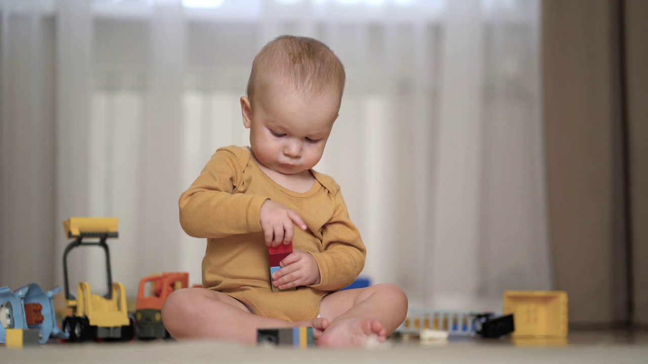 一个一岁的小男孩在家里玩五颜六色的积木，坐在地板上，享受游戏。视频下载